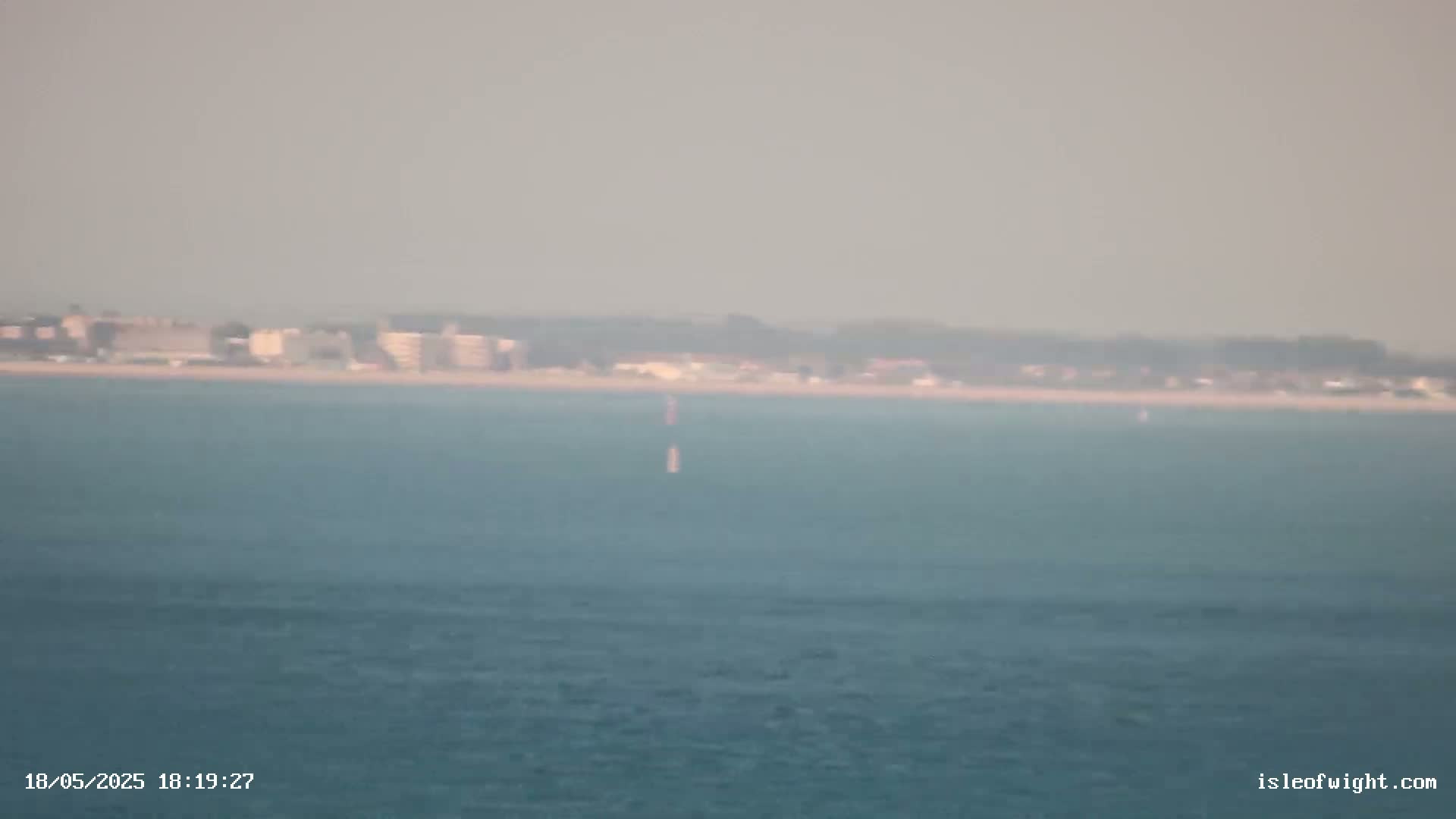 A hazy view shows a distant coastline with buildings and a calm body of water in the foreground.