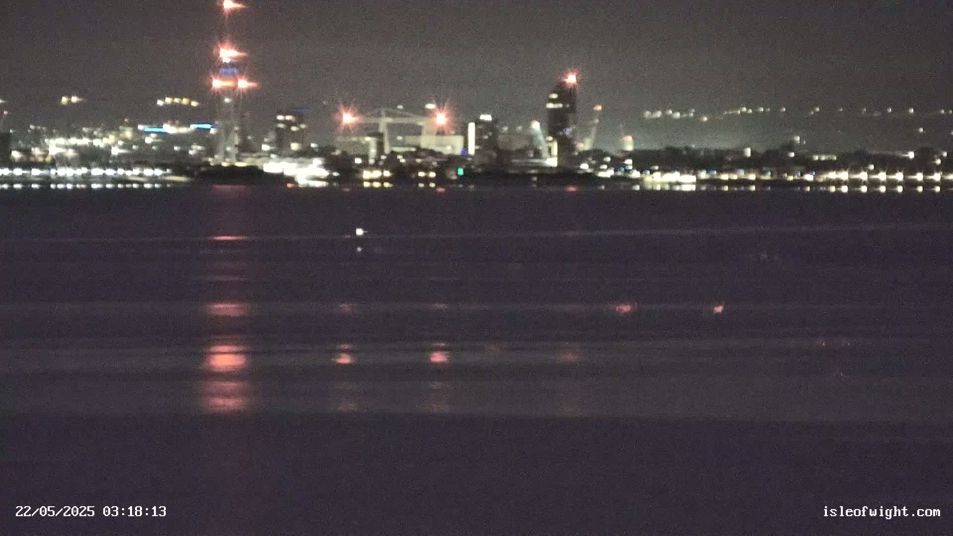 A nighttime view of a city skyline across a dark body of water, reflecting city lights.