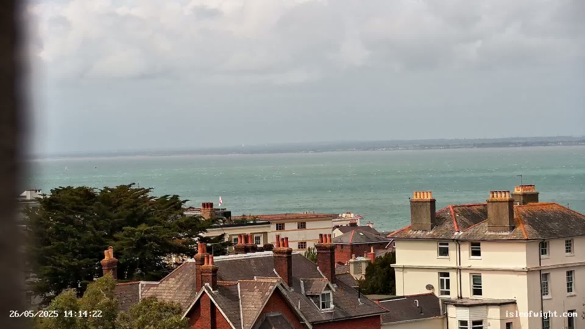 A view of a town's rooftops and a choppy sea under a cloudy sky.