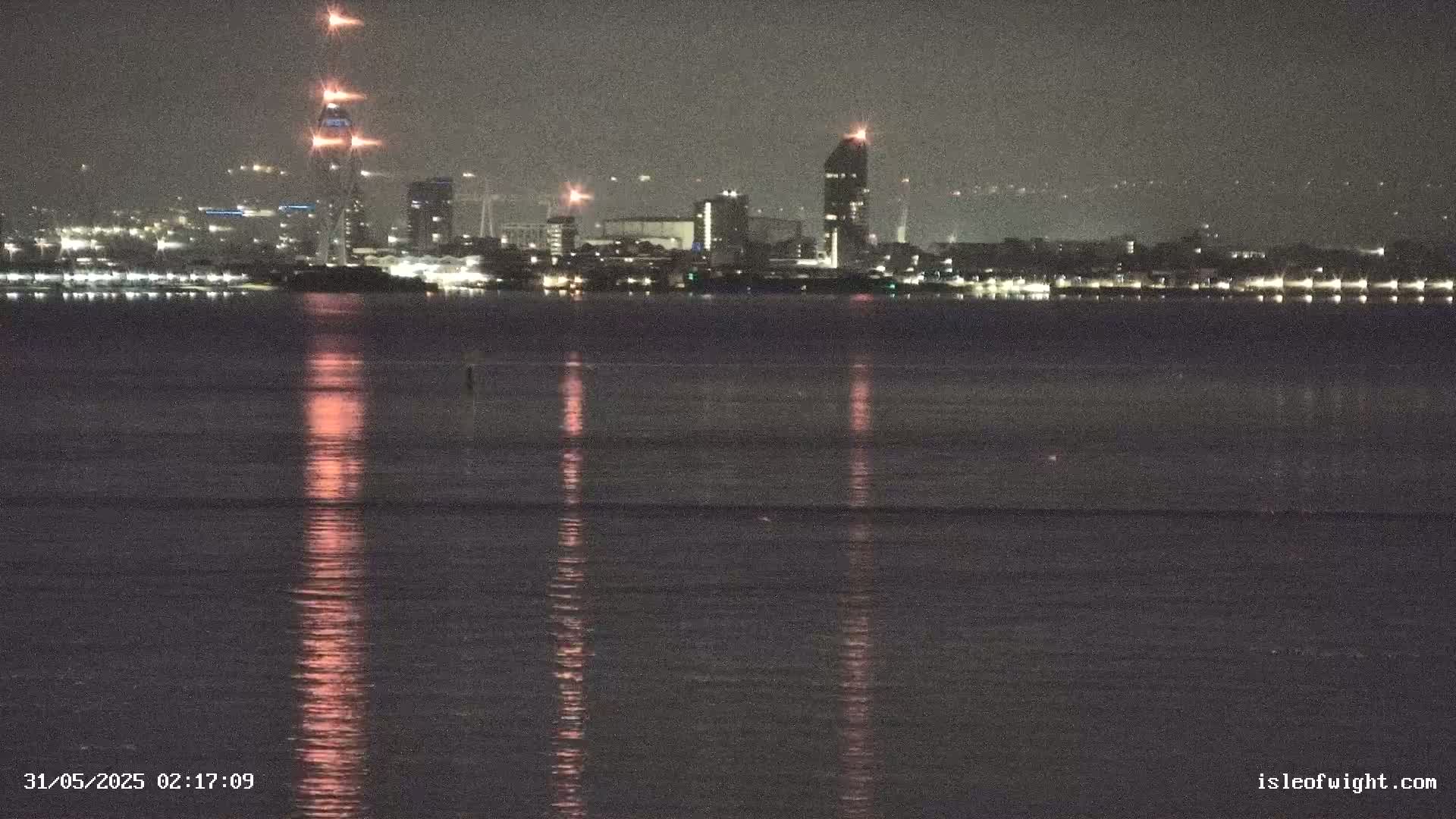 A nighttime view across a calm body of water reflecting the lights of a distant city skyline.