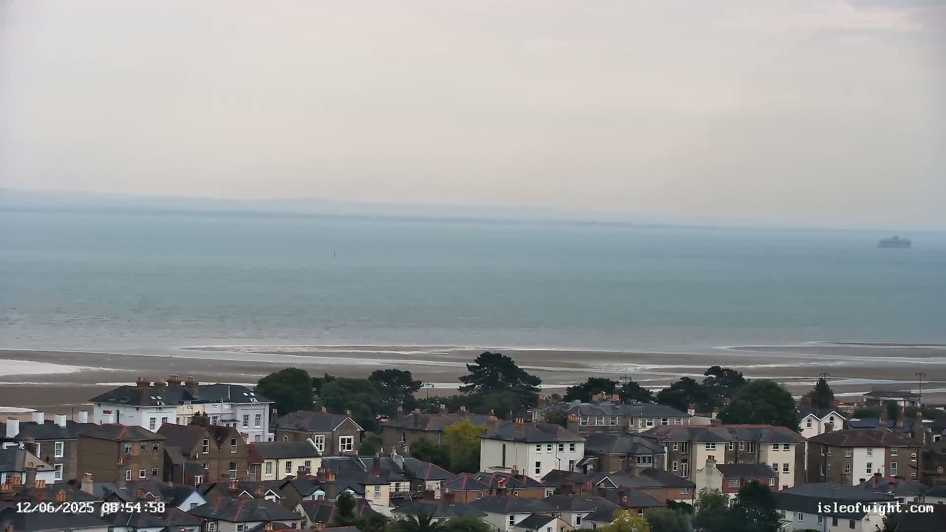 A coastal town overlooks a calm, hazy sea with a sandy shore in the distance.