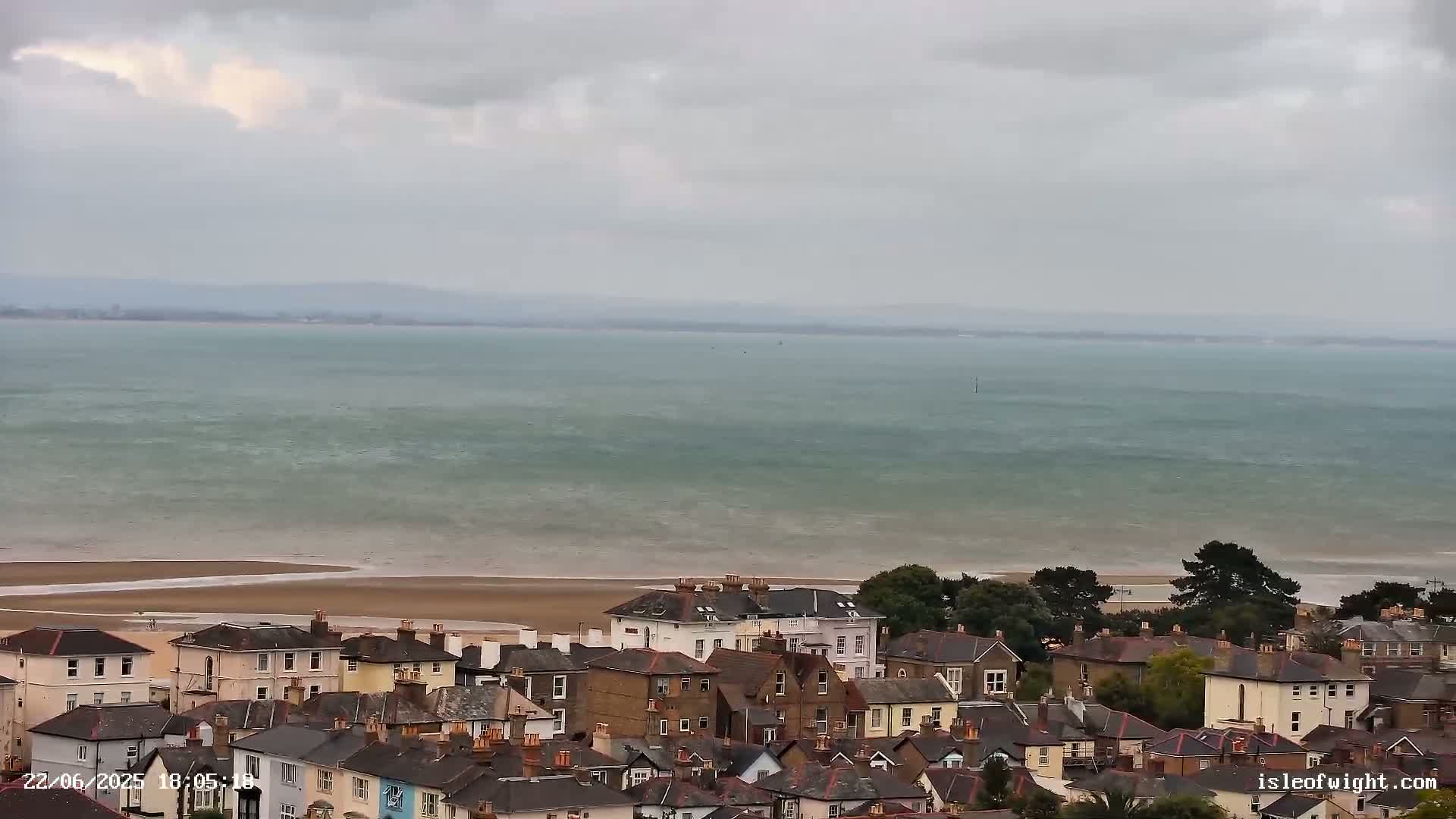 A coastal town with many houses is situated overlooking a calm, grey sea under an overcast sky.