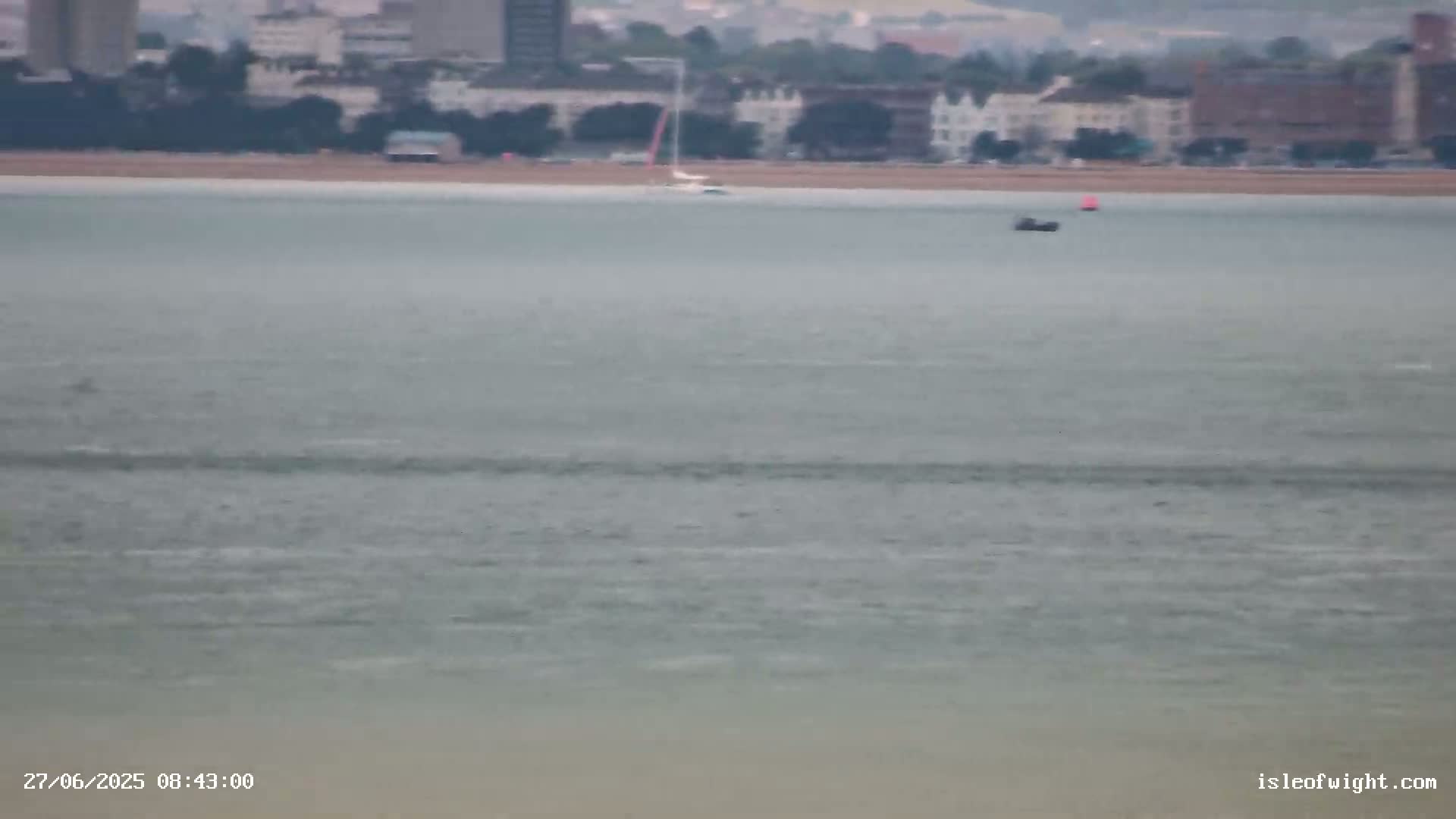 A calm body of water with a sailboat and a small boat visible in the distance, under an overcast sky.