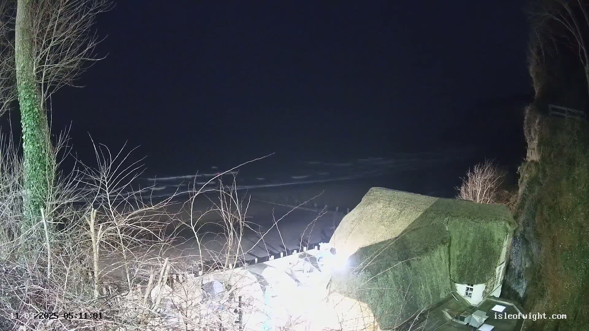 A thatched-roof house sits on a cliff overlooking a dark, wavy sea at night.