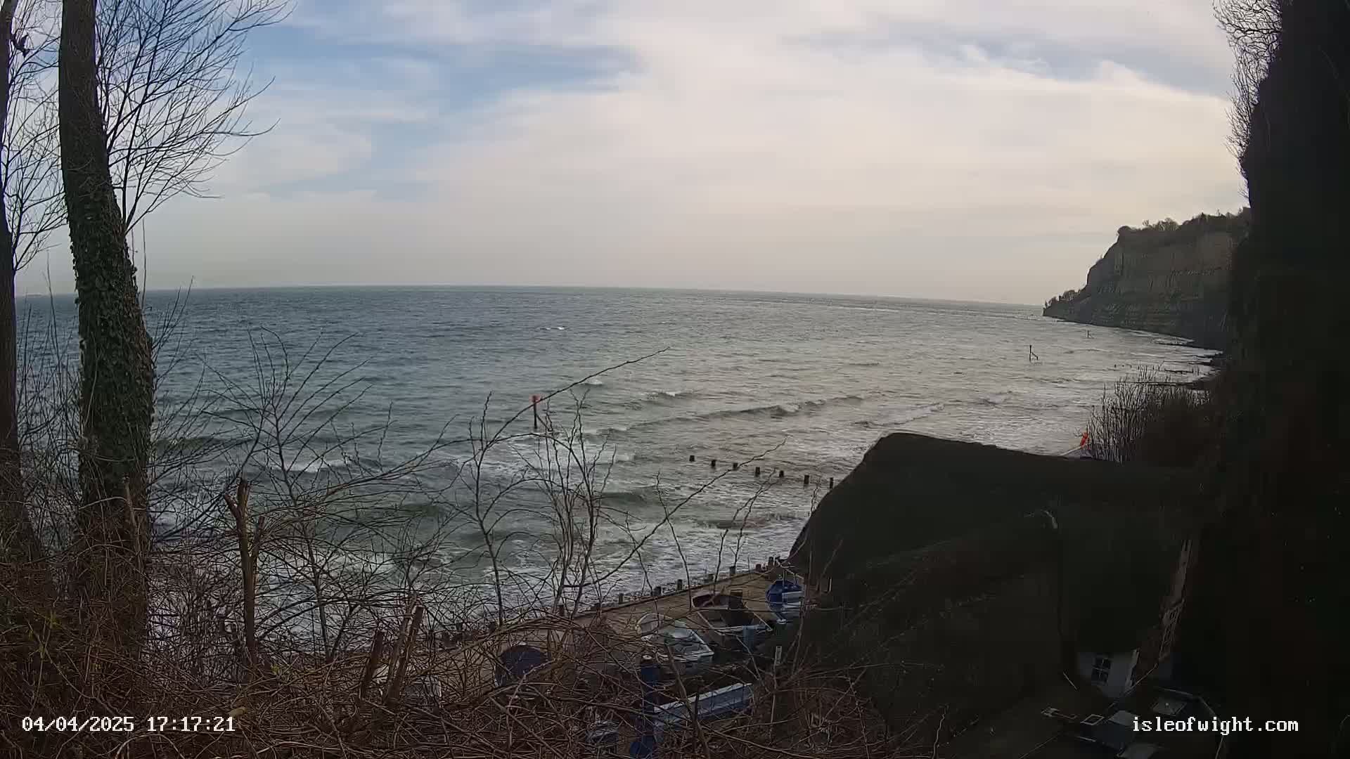 A rocky coast with several small boats in a cove is viewed from above, with a gray and somewhat choppy sea under a cloudy sky.