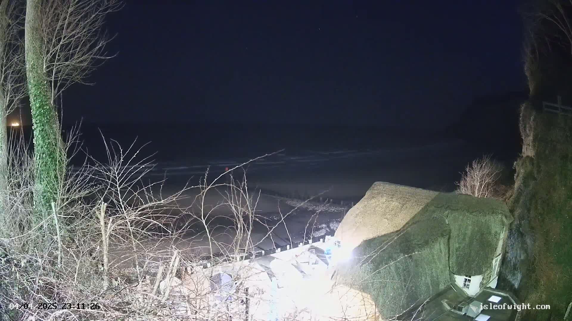 A thatched-roof house sits on a cliff overlooking a dark, wavy ocean at night.