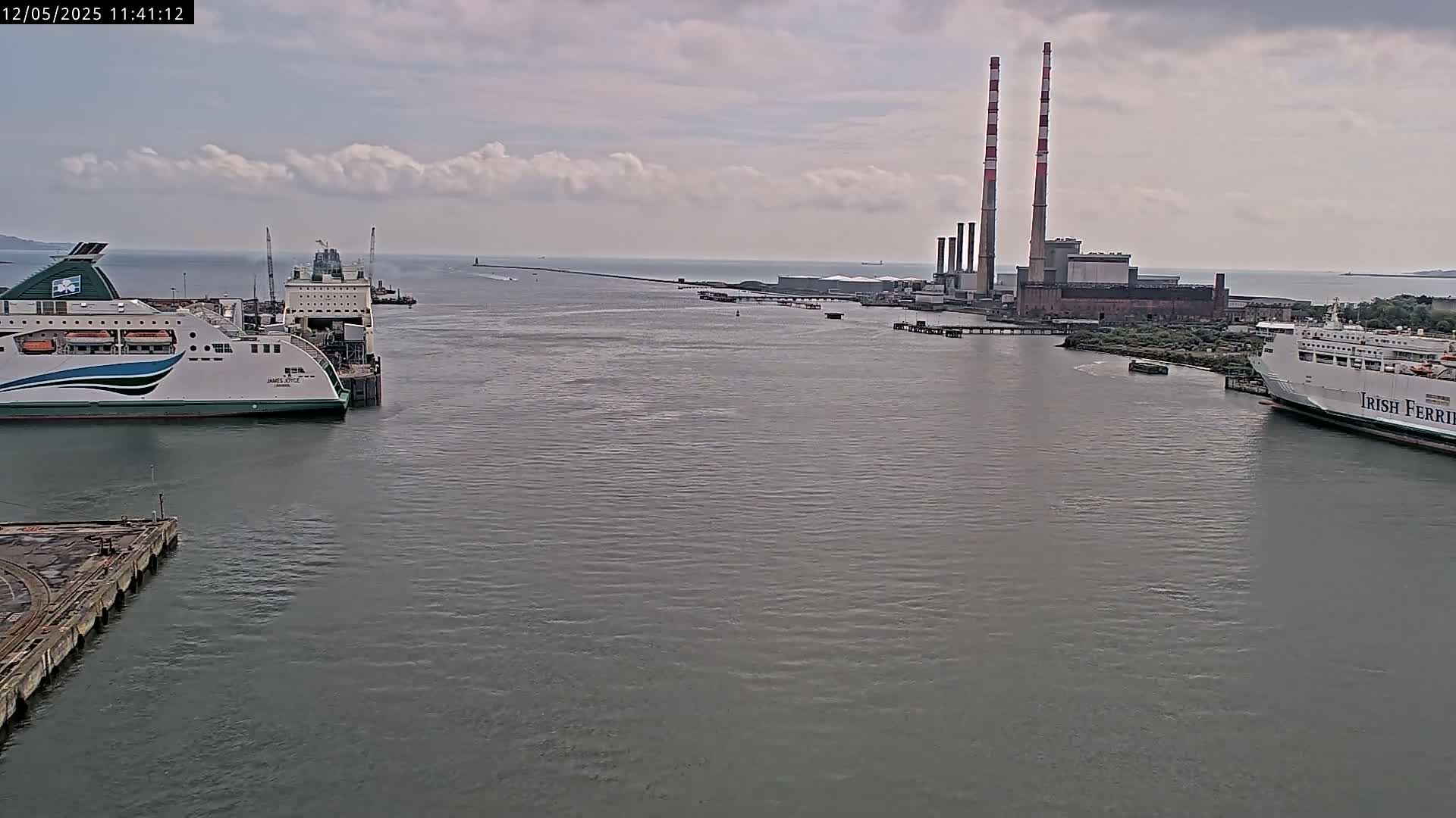 Two ferries are docked near a power plant on a cloudy day.