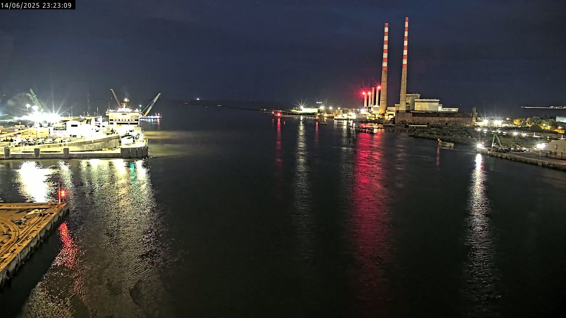 A large ship is docked at a port next to an industrial area with tall smokestacks under an overcast sky.