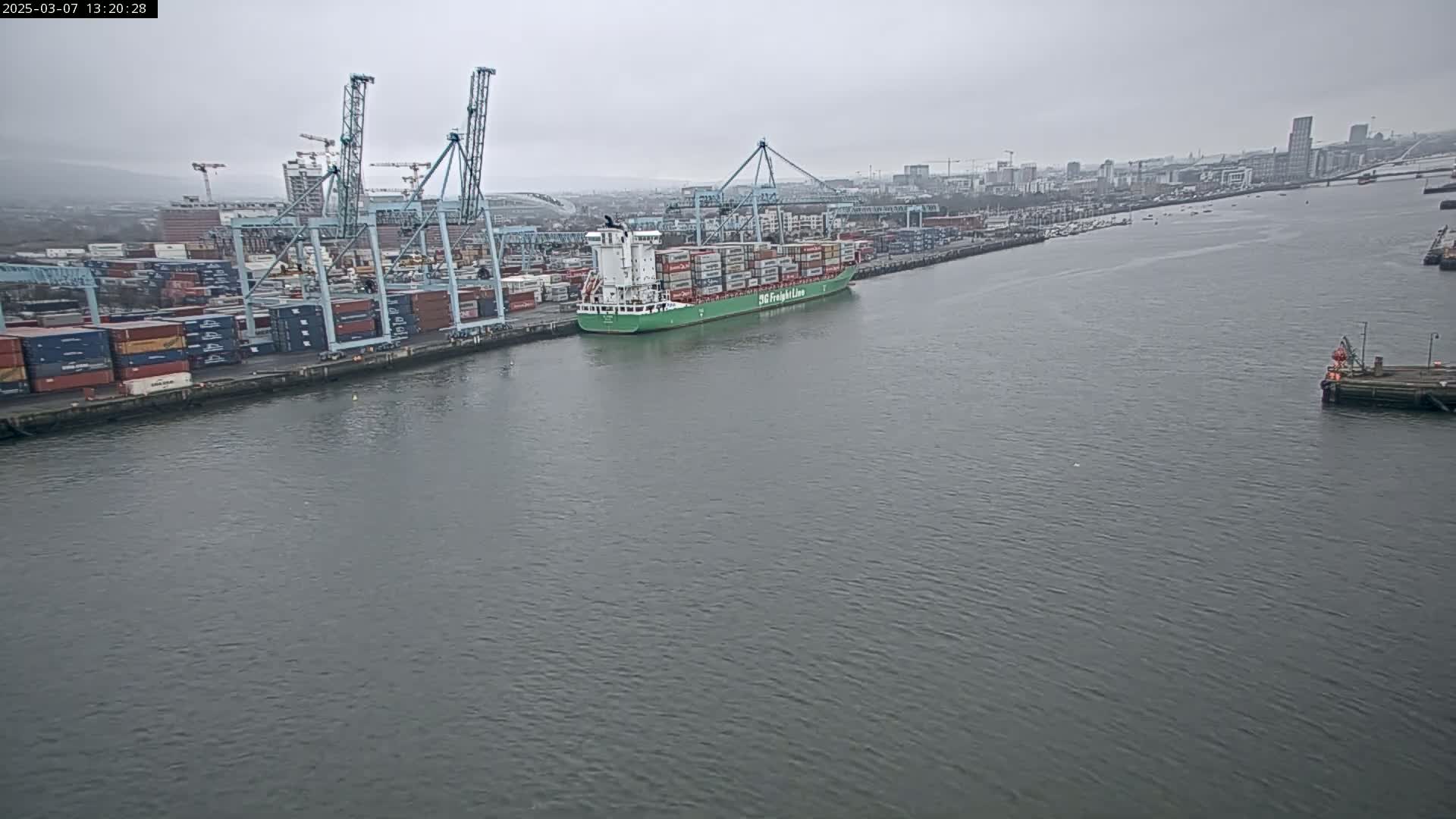 A large container ship is docked at a port on an overcast day.