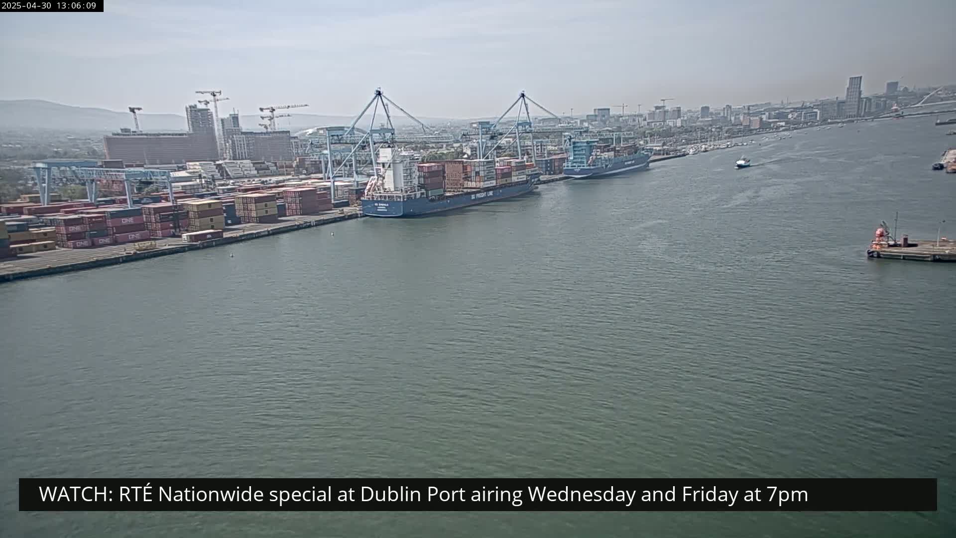 Two large container ships are docked at a harbor on a partly cloudy day.