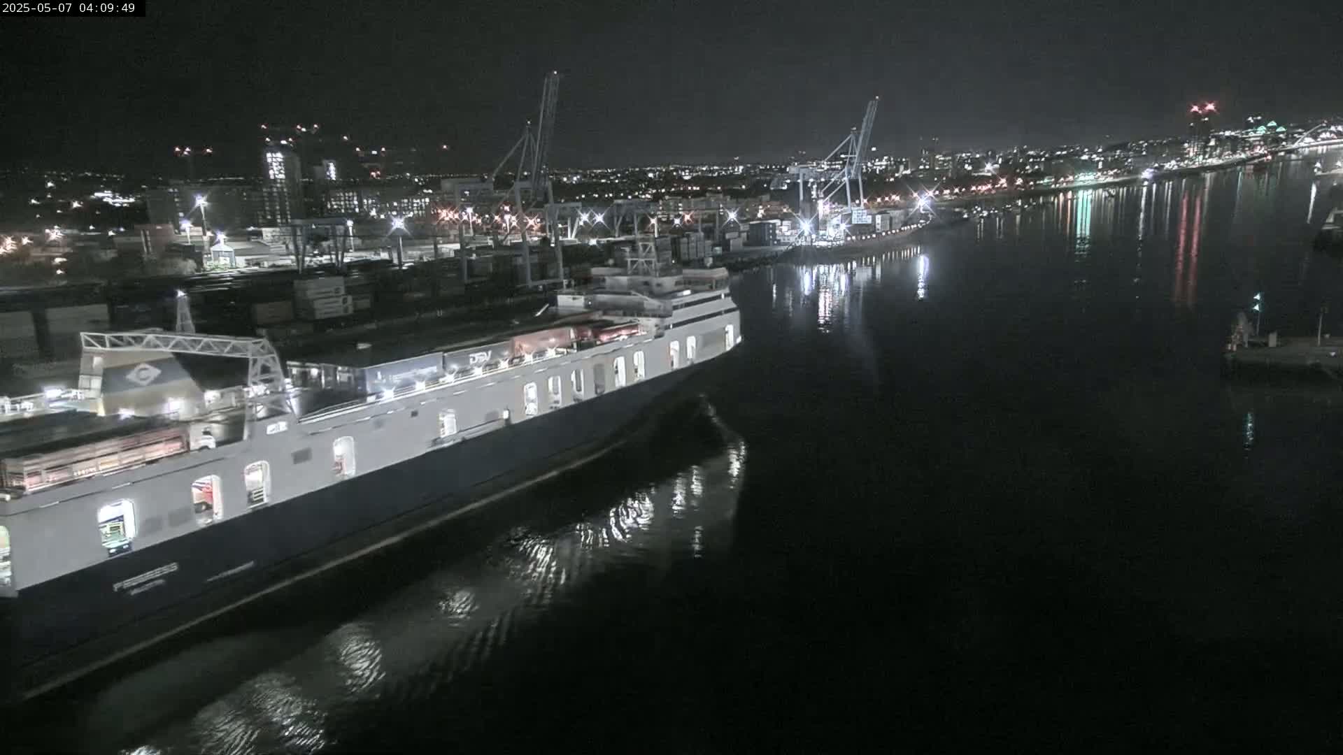 A large ferry is docked at a nighttime port, with calm water reflecting the city lights.