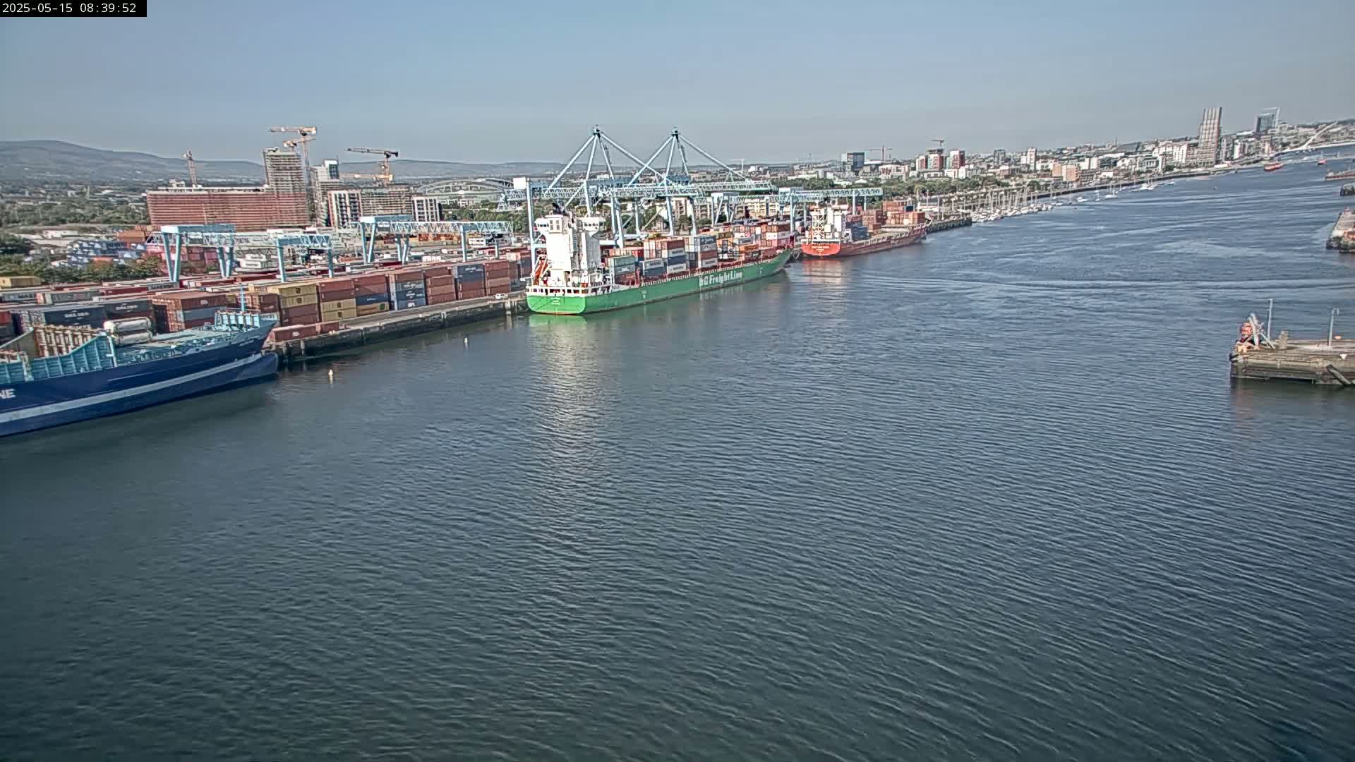 Several large container ships are docked at a port on a calm, sunny day.