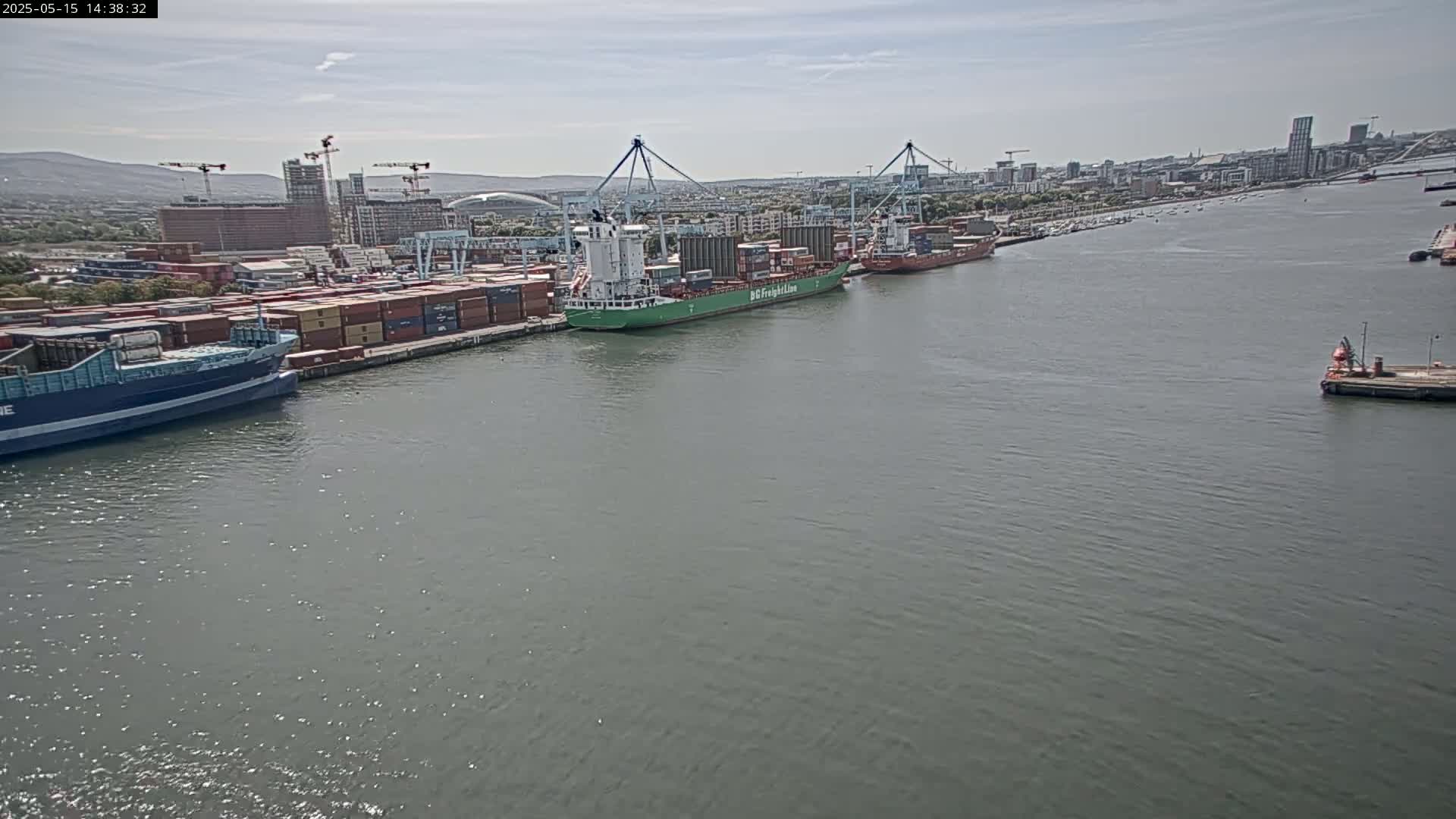 Several container ships are docked at a port on a calm, overcast day.