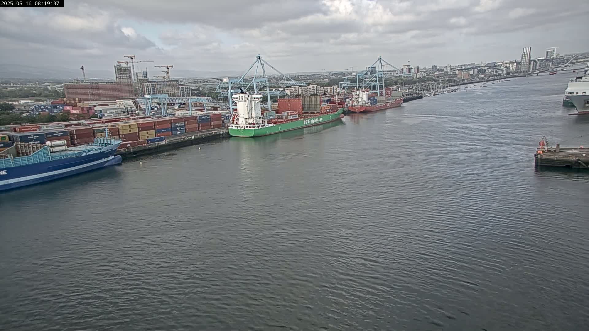 Several container ships are docked at a port under a cloudy sky.