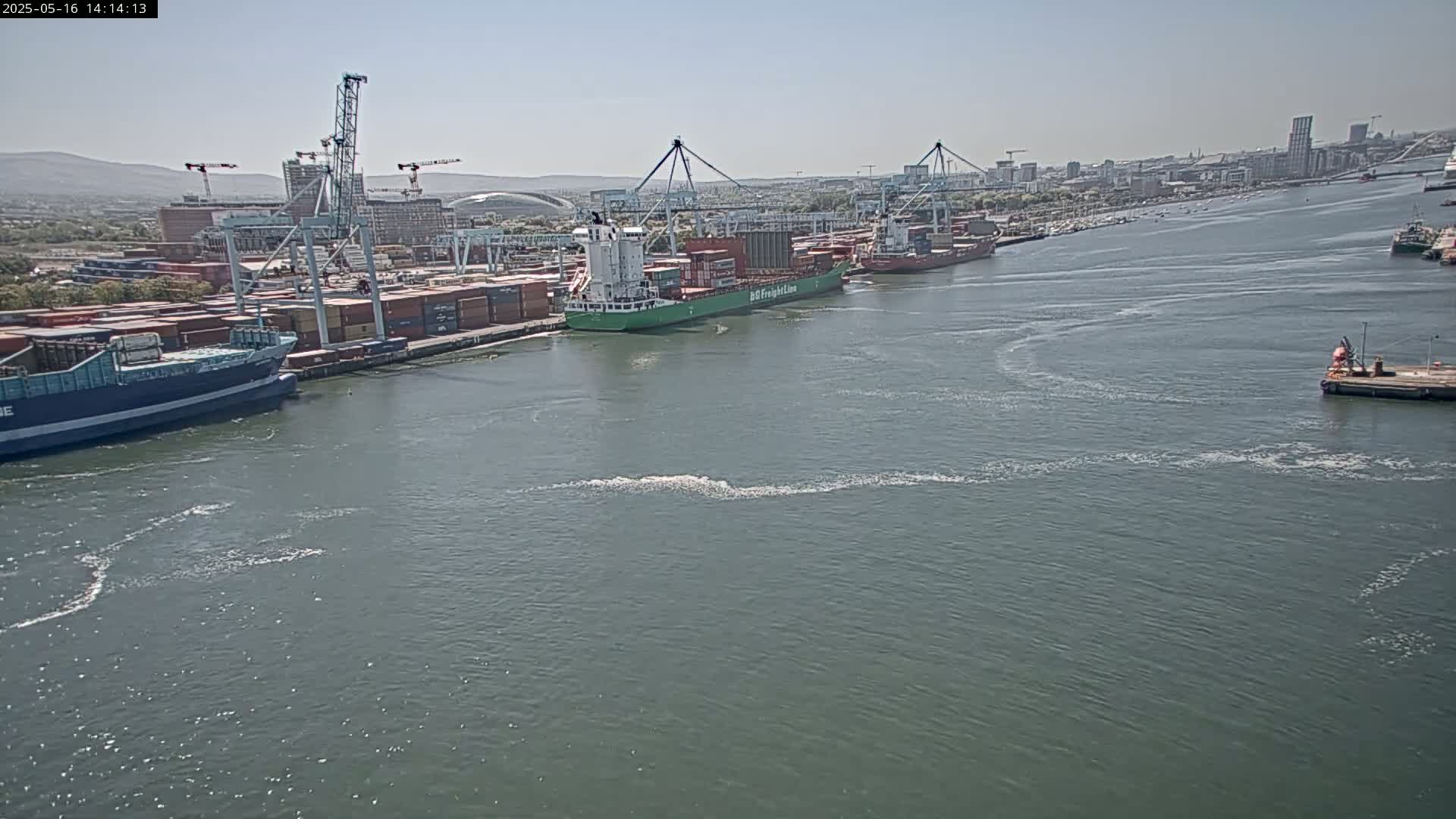 Several container ships are docked at a busy port on a calm, sunny day.
