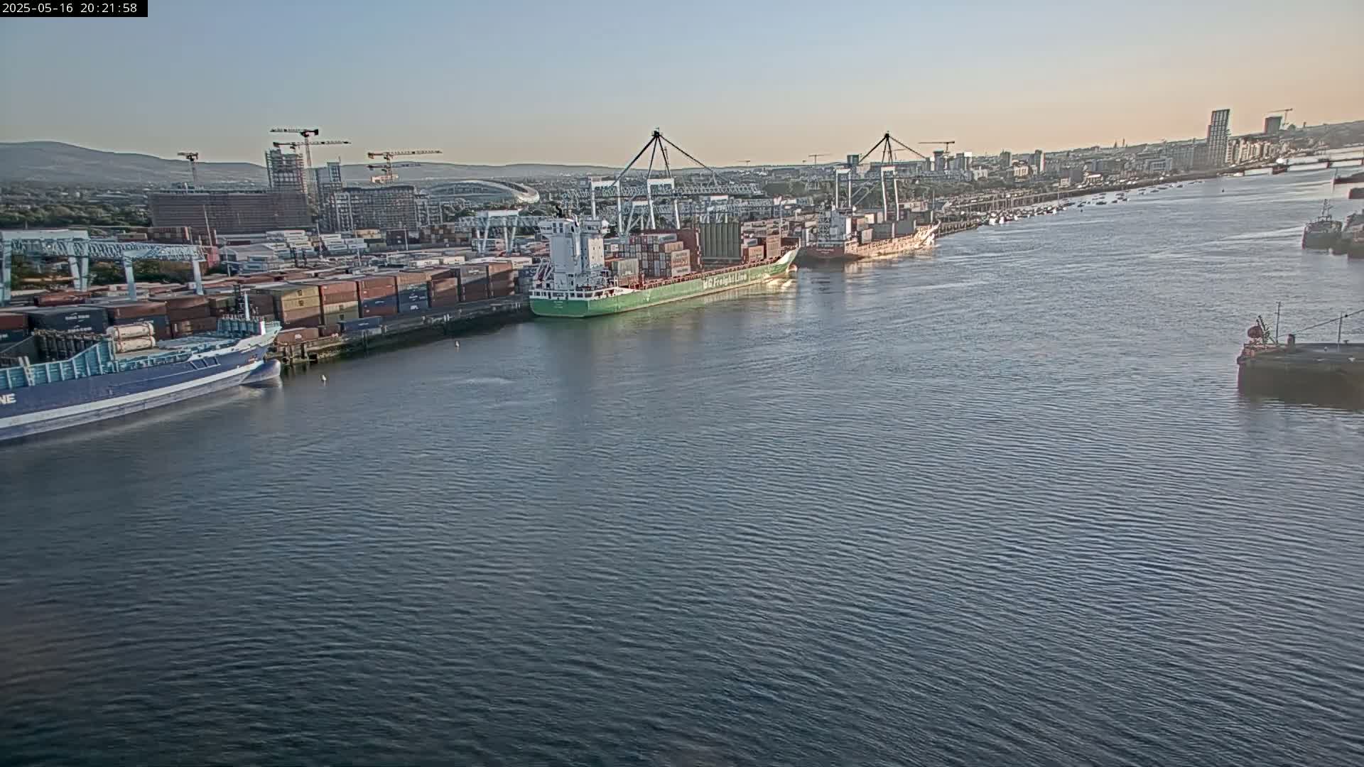 Several container ships are docked at a port under a clear, twilight sky.