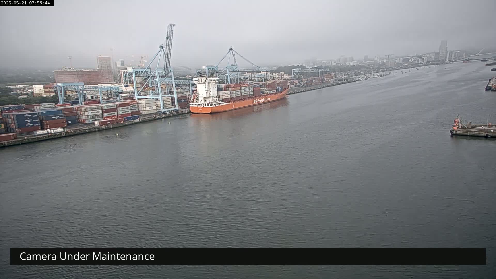 A large container ship is docked at a port on an overcast day.