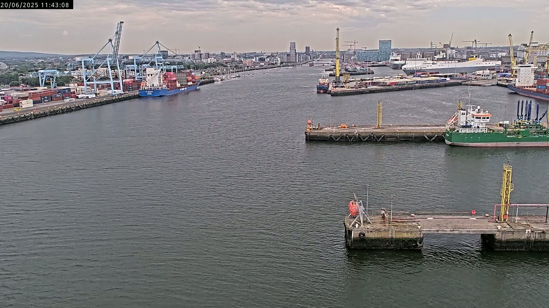 A wide shot of a harbor on an overcast day shows several ships, cranes, and docks.