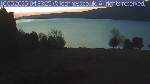 A calm body of water is visible at sunrise, silhouetted by dark trees and hills in the foreground.