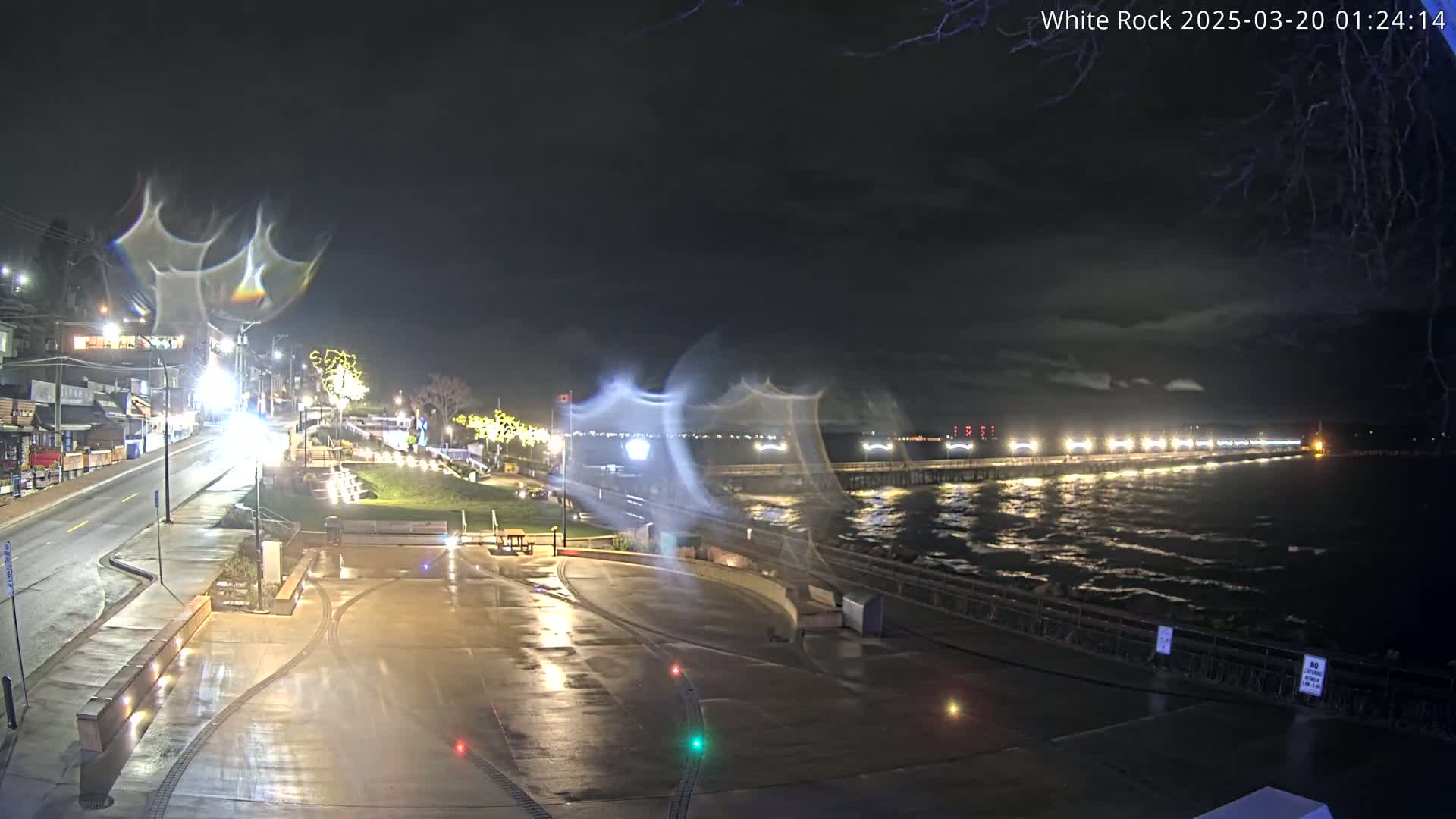 A nighttime view of a wet waterfront area with a pier extending into a choppy sea under a partly cloudy sky.