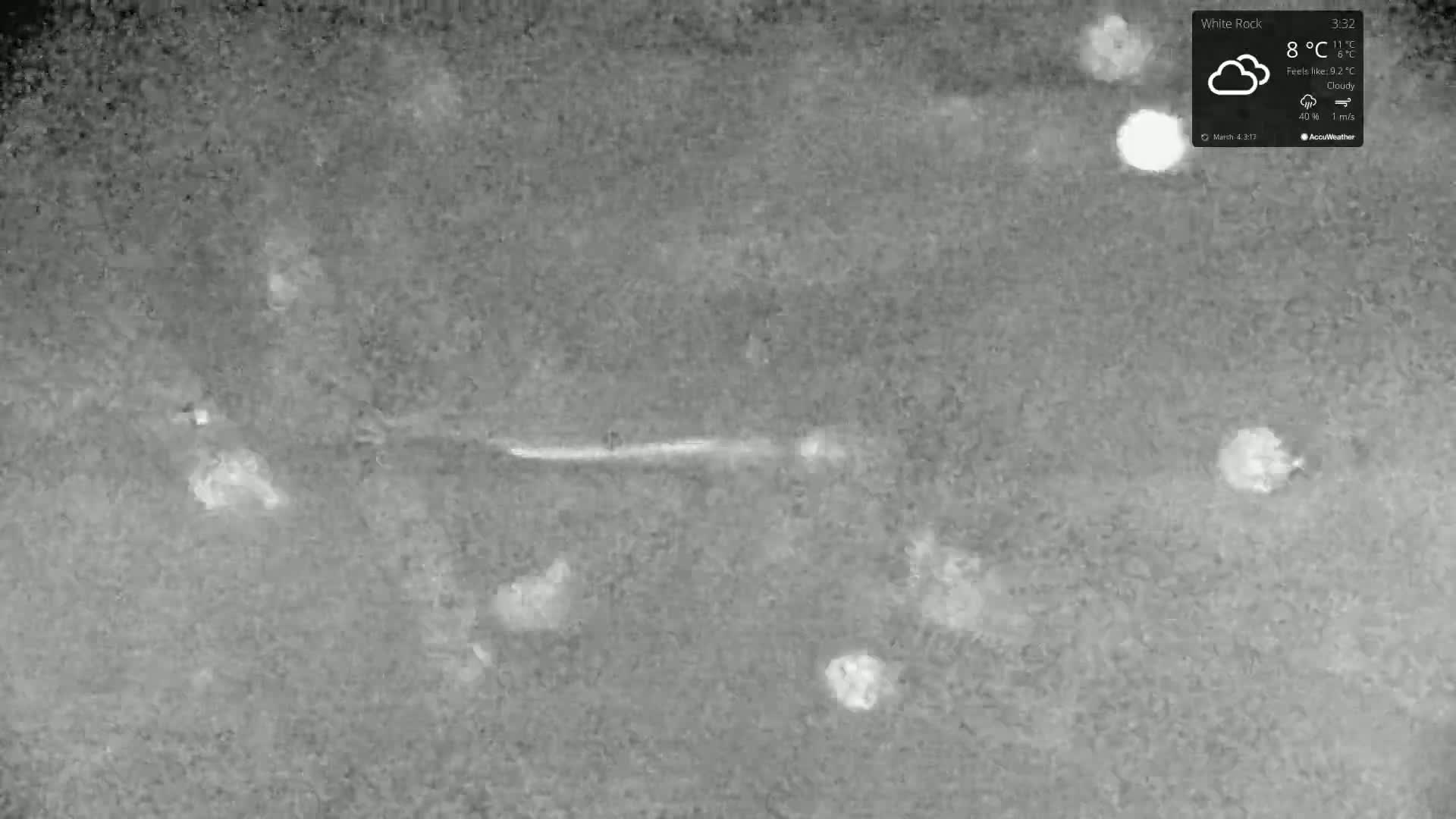 A grainy, thermal image shows several bright, circular shapes scattered across a darker gray surface under cloudy conditions.