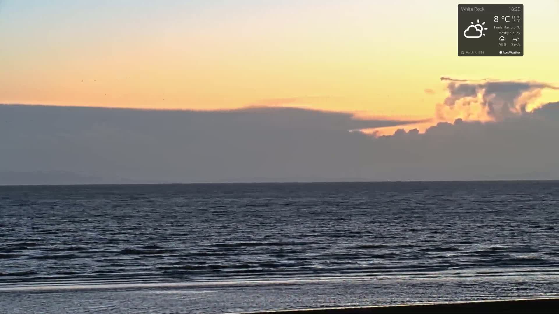 A mostly cloudy sunset over a calm ocean with a sandy beach in the foreground.