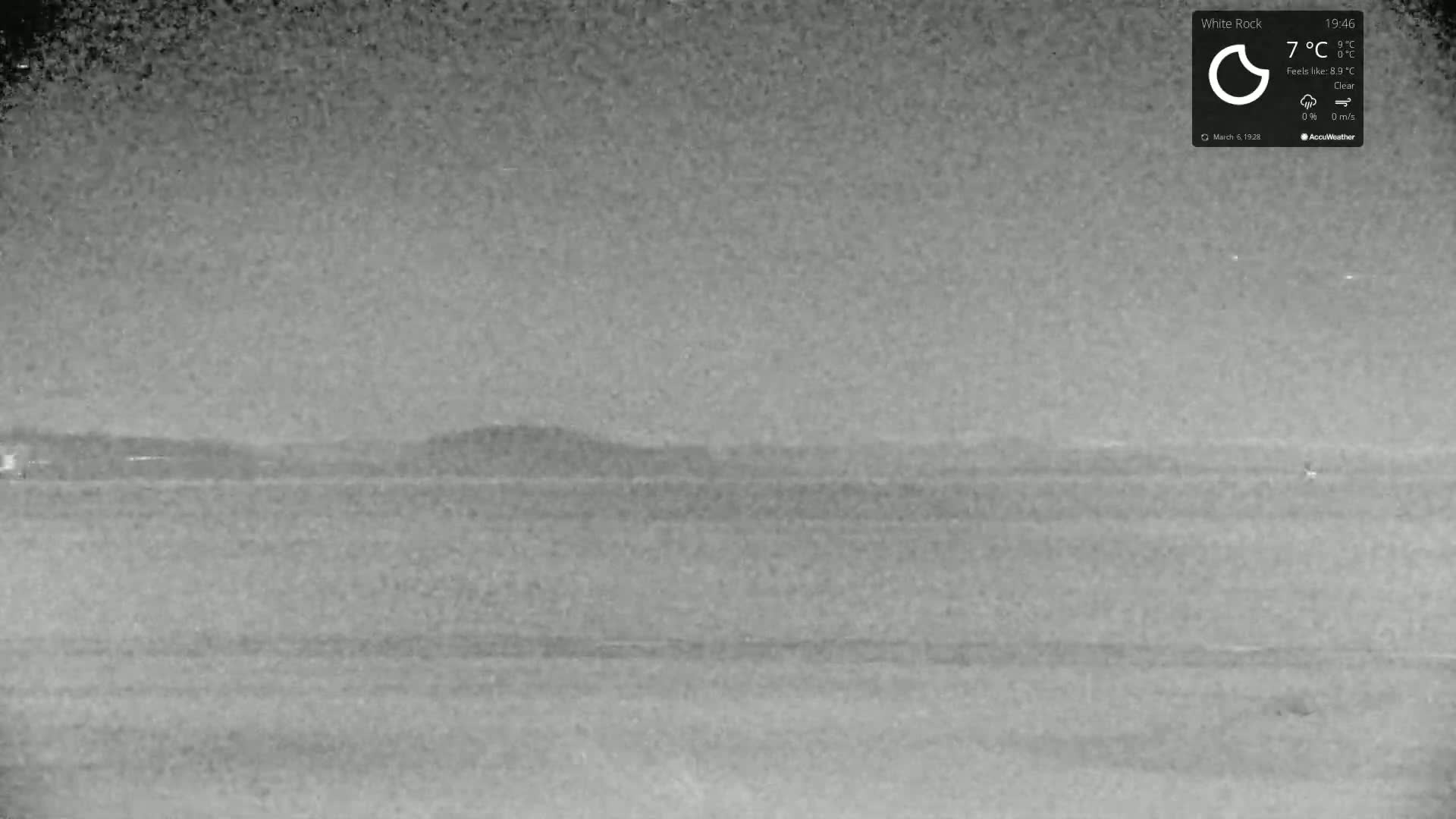 A nighttime, clear, and calm view shows a flat expanse of land extending to a distant, low-lying hill or ridge.