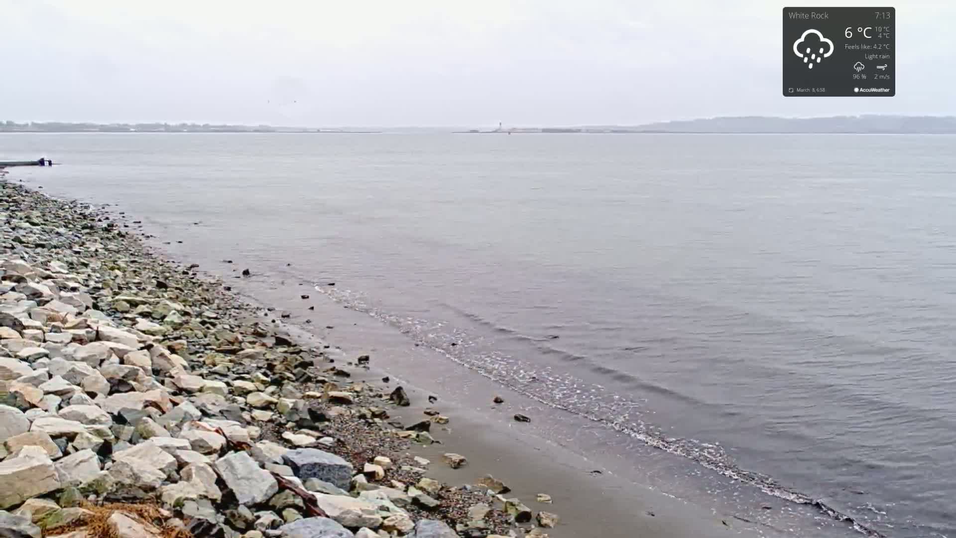 A rocky shoreline meets a calm body of water under a light rain.
