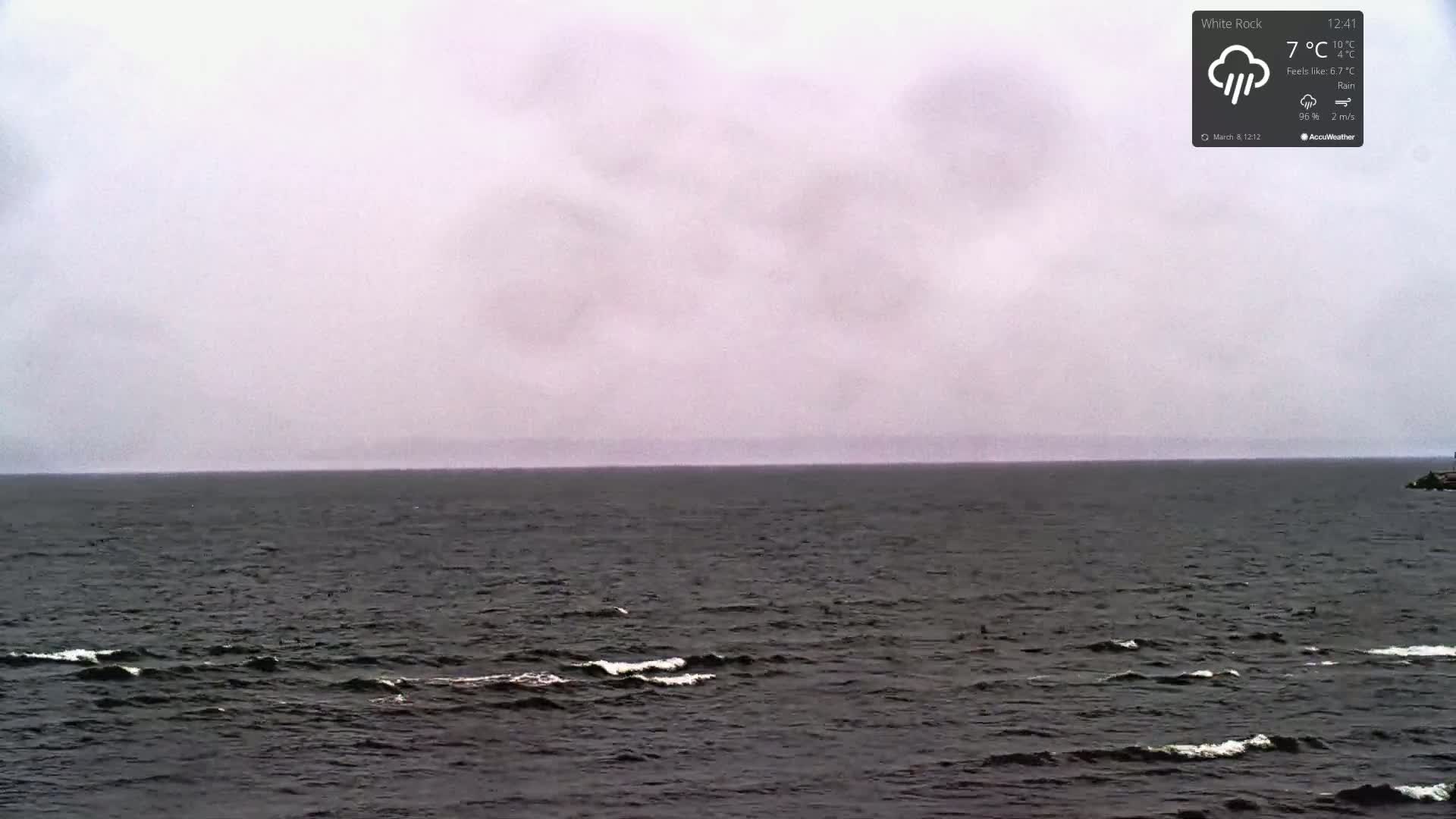 A dark, choppy sea stretches to a hazy, overcast horizon under a gray sky with rain.