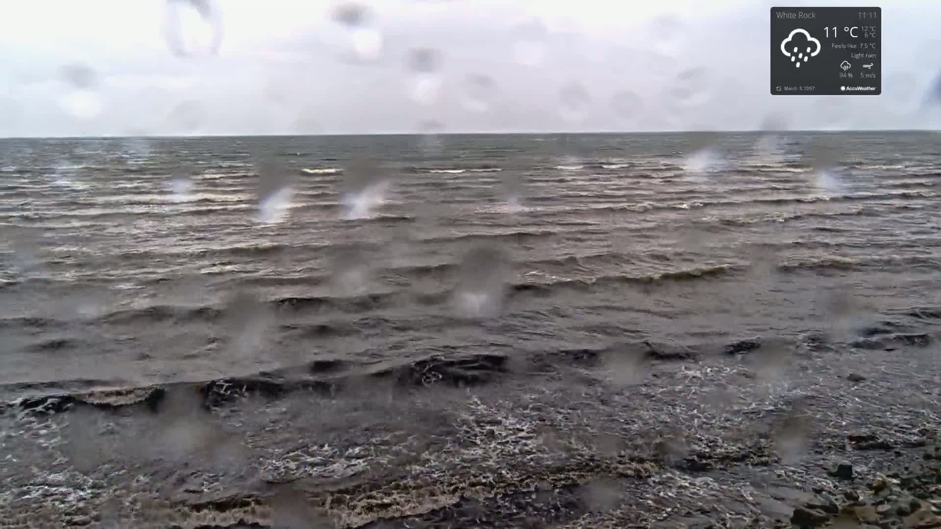A dark, choppy sea is seen through rain-covered glass under a gray sky.