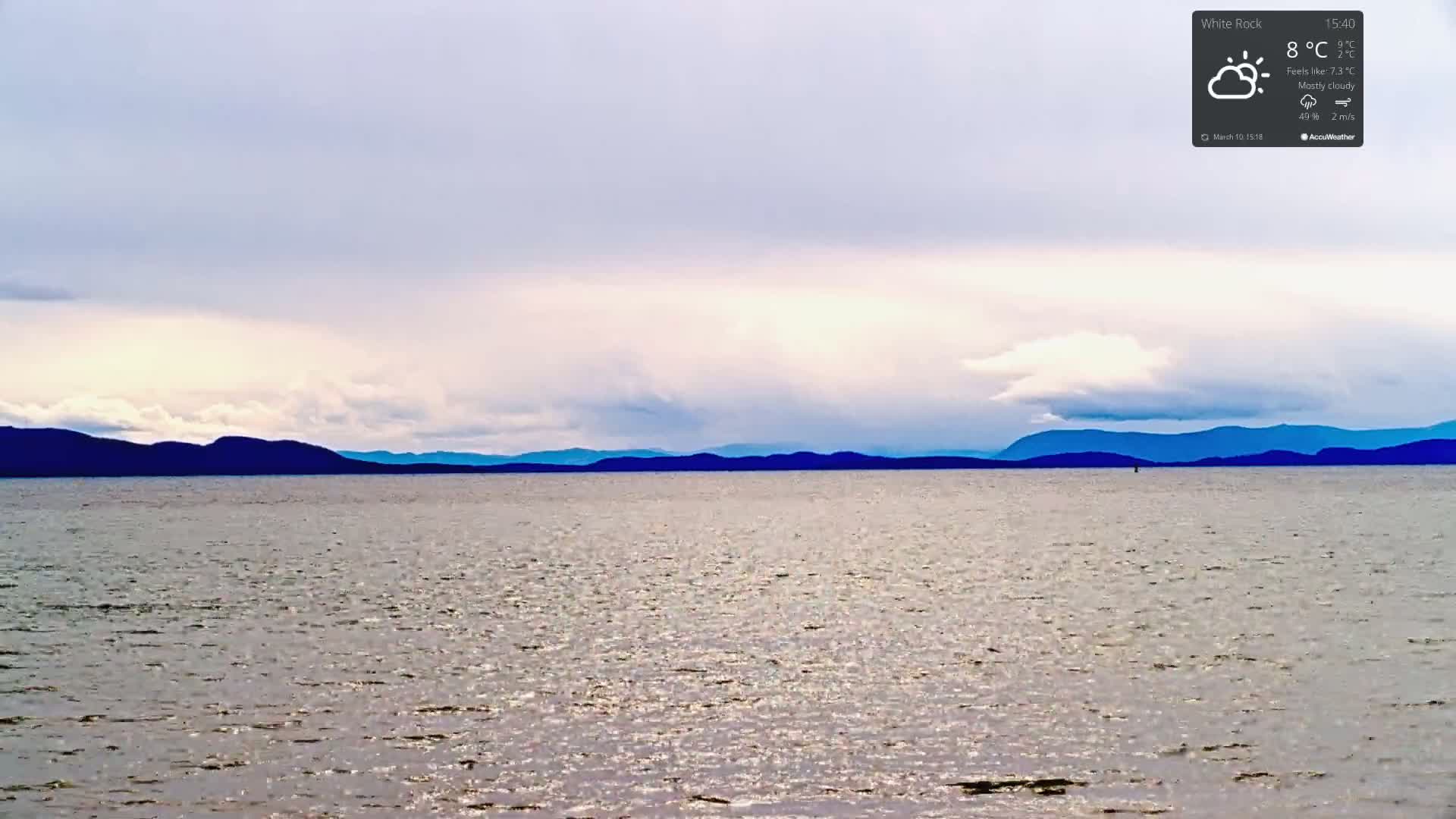A mostly cloudy sky hangs over a calm body of water, with dark mountains visible on the horizon.