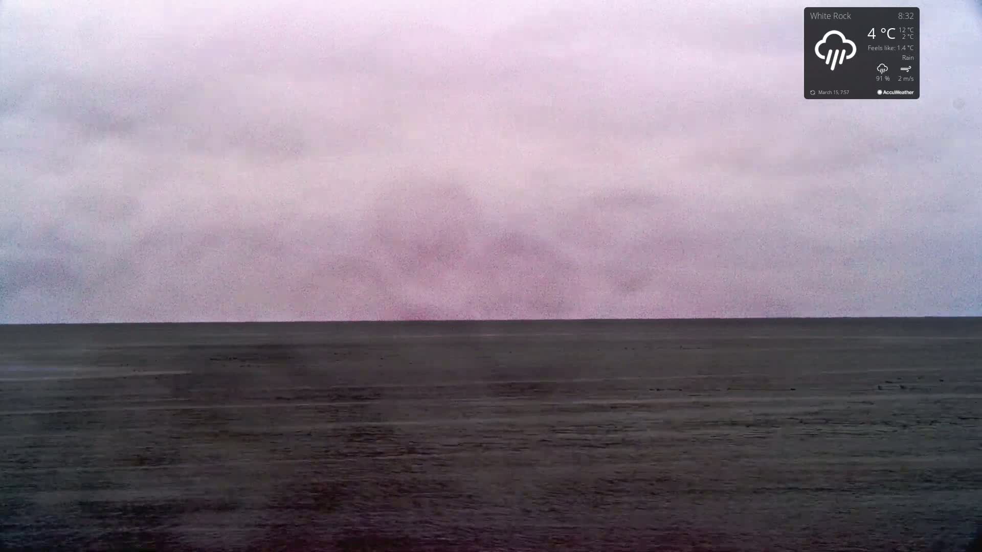 A dark, flat expanse of water meets a cloudy, purplish-grey sky under rainy conditions.