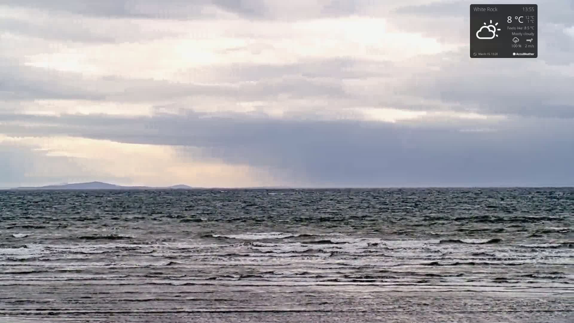 A mostly cloudy sky over a dark, wavy sea with a distant shoreline.