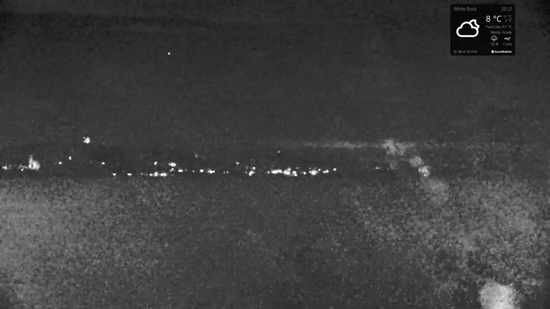 A nighttime, mostly cloudy scene shows a distant line of lights possibly from a town or city under an 8°C sky.