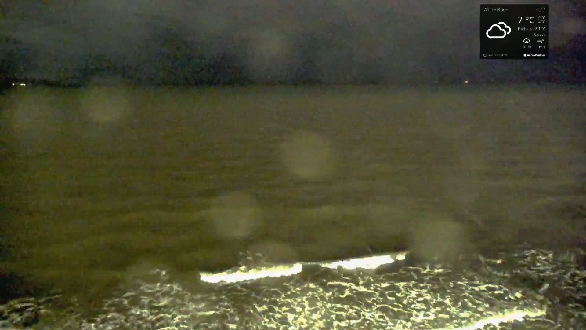 A nighttime, cloudy view of choppy water with small waves illuminated by a light source.