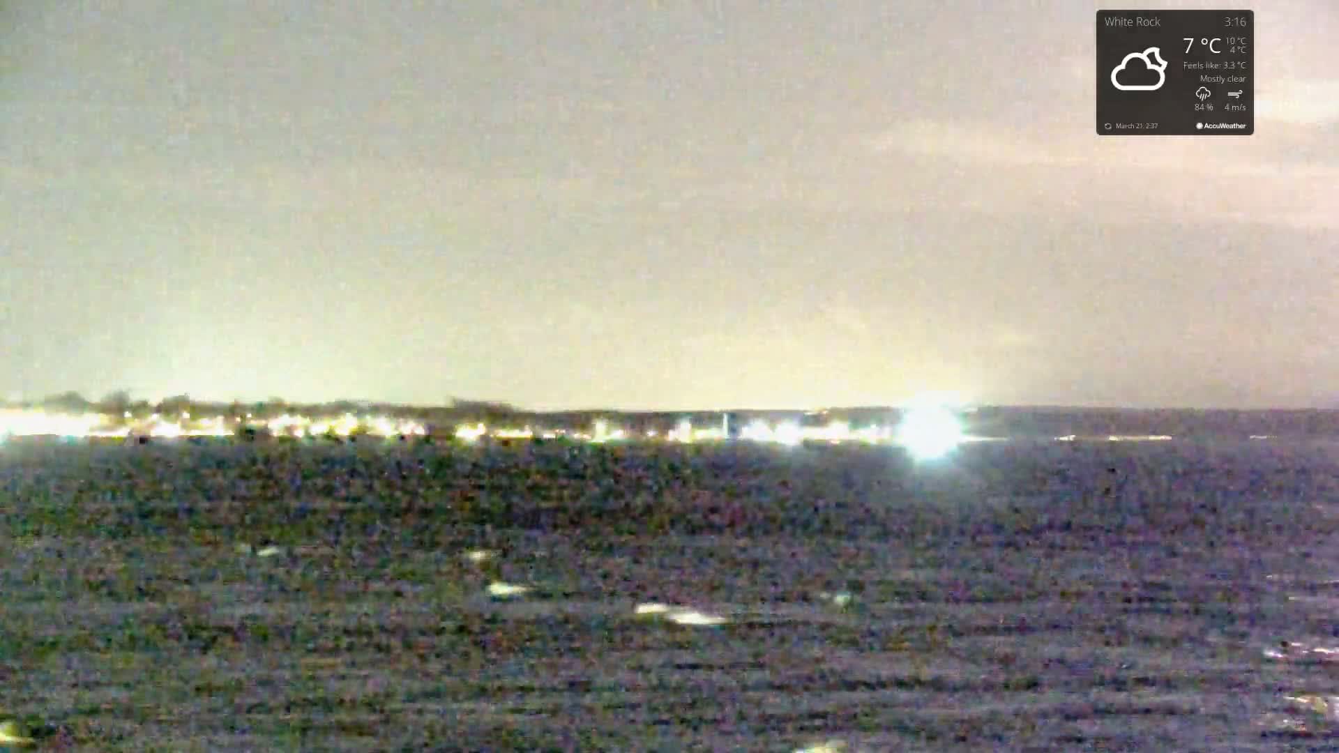 A mostly clear night shows a dark body of water with a distant, faintly lit shoreline.