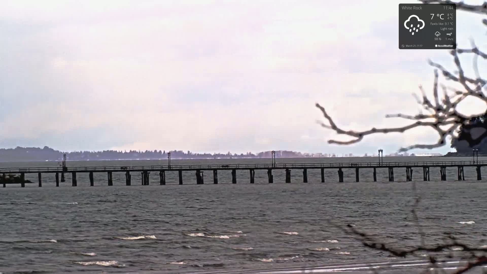 A long pier extends over a choppy gray sea under a cloudy sky with light rain.