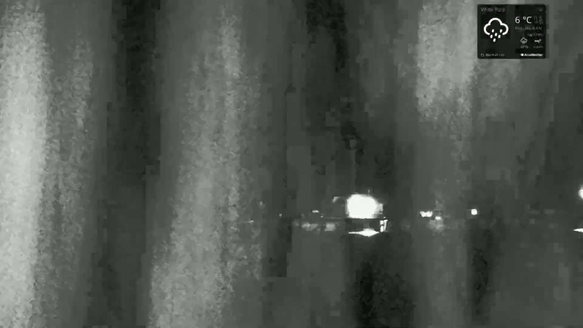 A nighttime, low-light image shows blurry shapes of vehicles driving through rain.