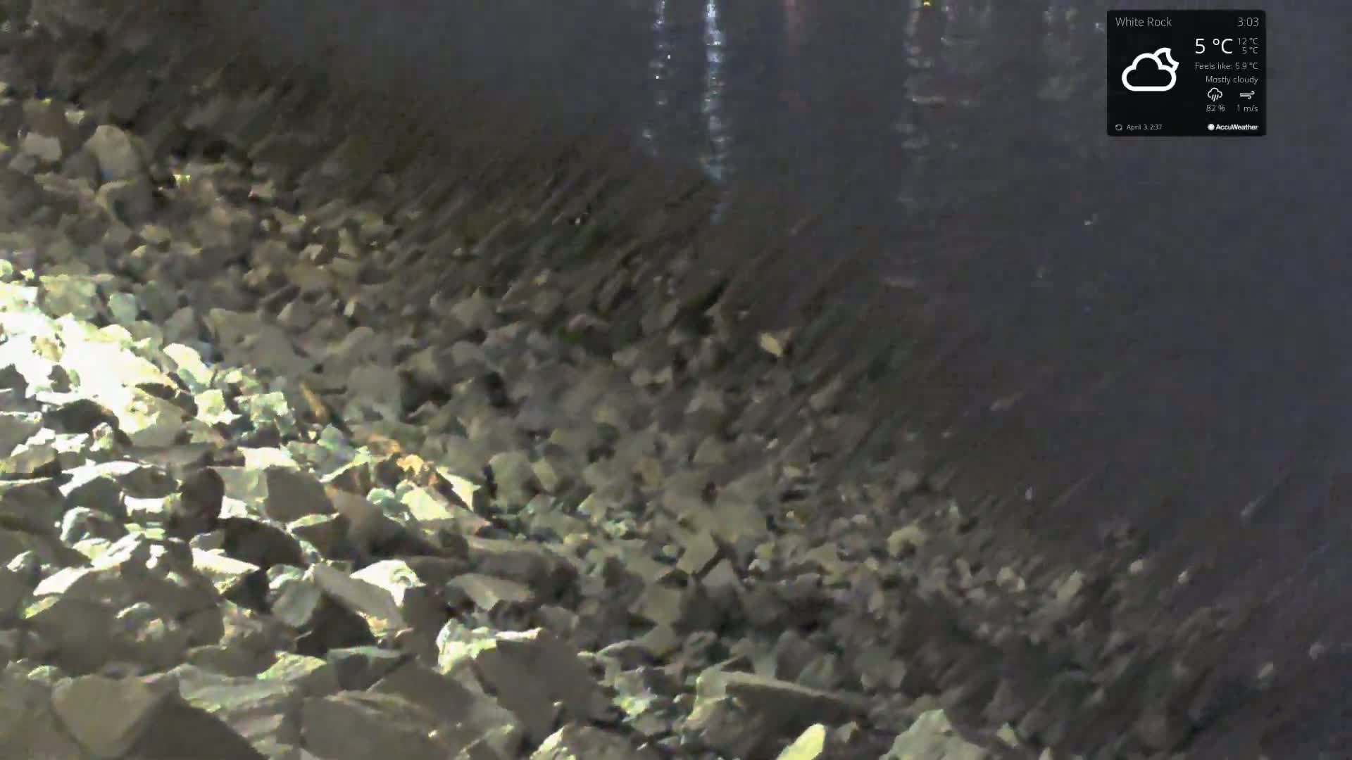 A rocky shoreline is visible at night under mostly cloudy skies.
