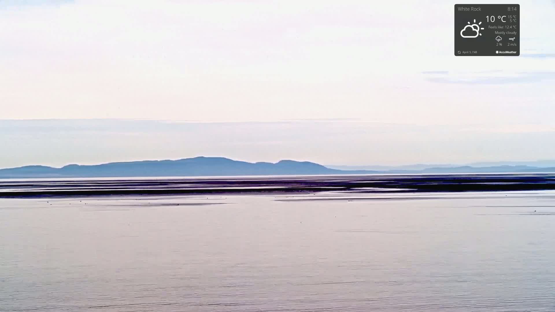 A mostly cloudy day with a calm sea shows a distant mountain range under a pale sky.