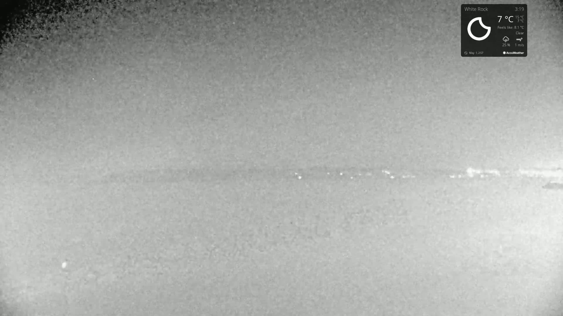 A low-light, nighttime image shows a clear, flat horizon with a faint line of lights in the distance under a clear sky.