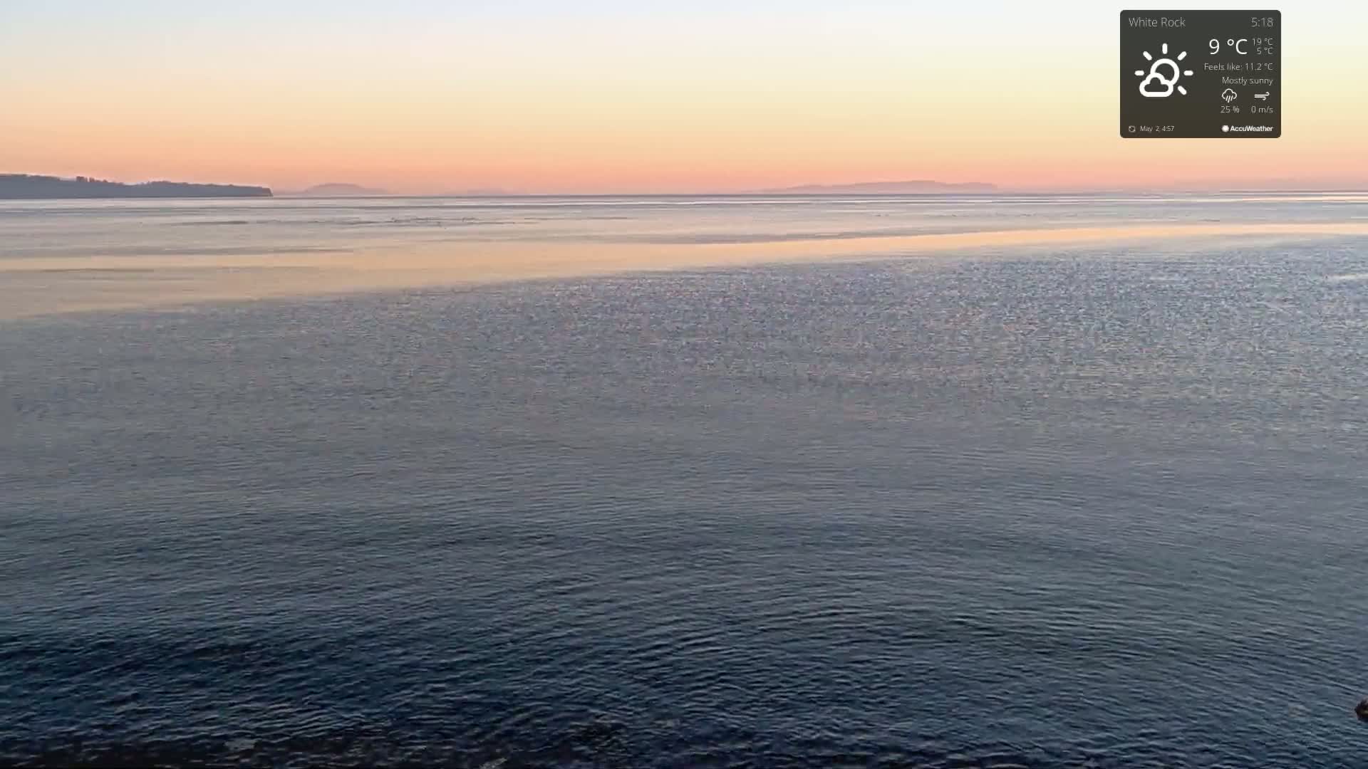 A mostly sunny sunset over calm water with a distant shoreline.