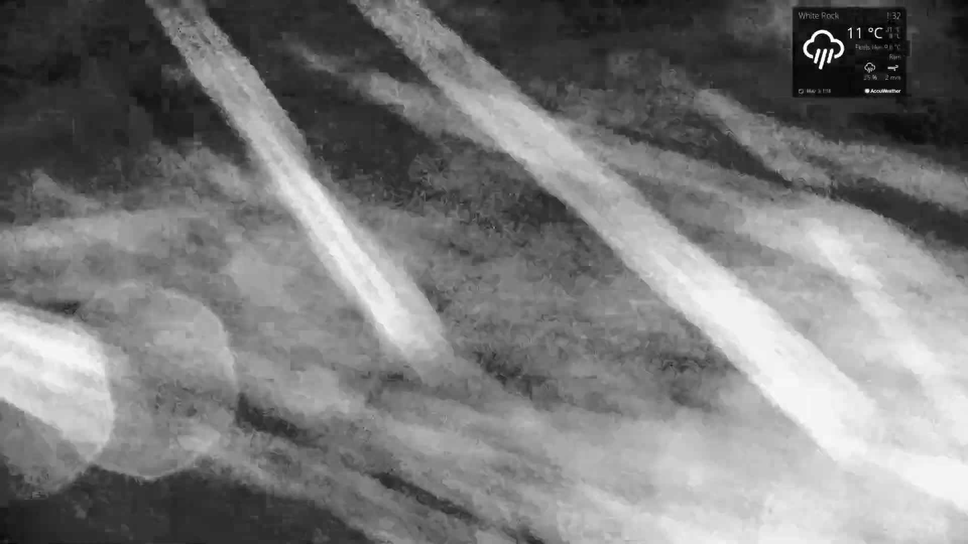 A grayscale image shows streaks of light against a dark, textured background under rainy, 11°C weather conditions.