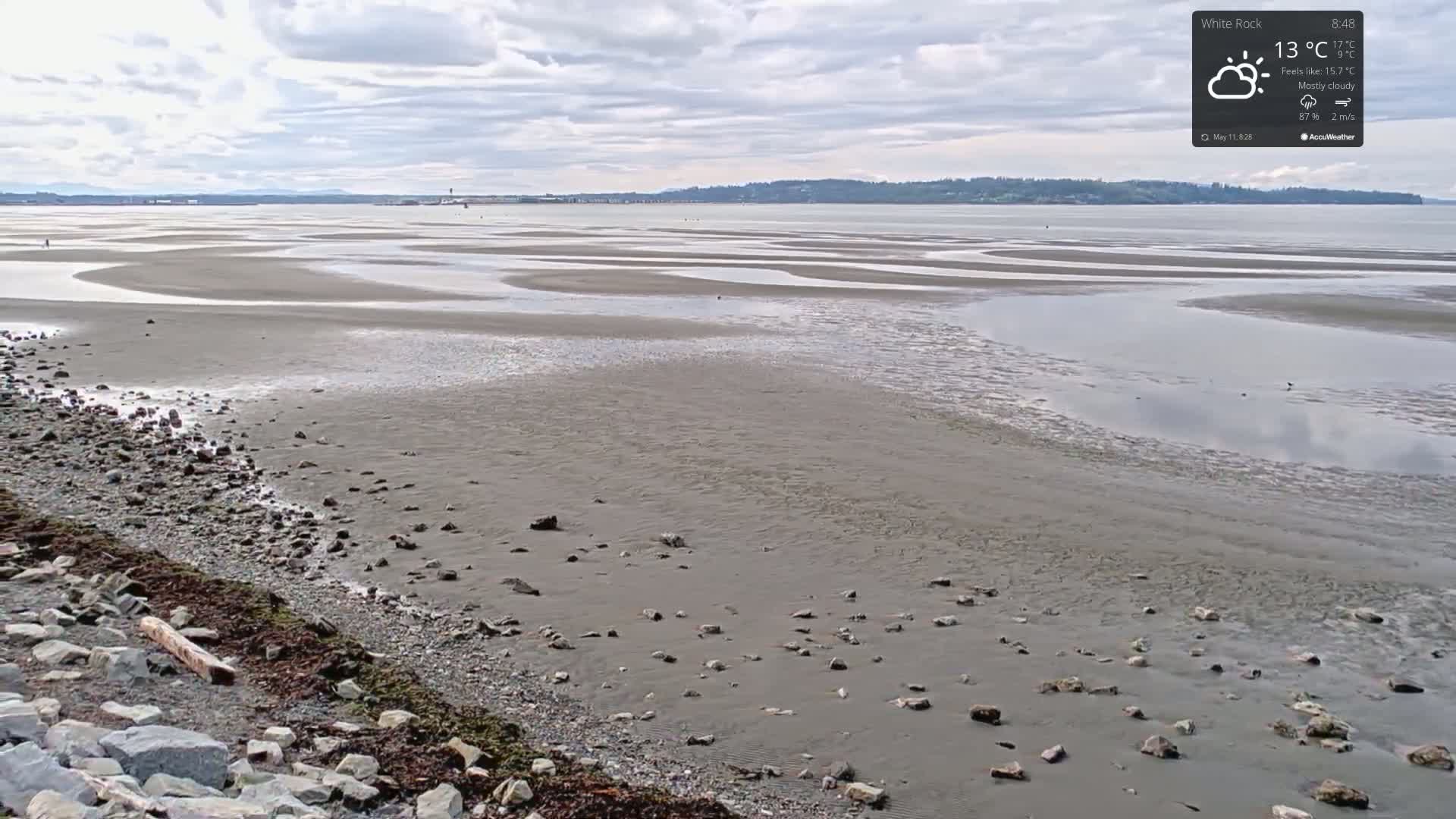 A mostly cloudy sky overlooks a wide expanse of tidal flats, with a rocky shoreline in the foreground.