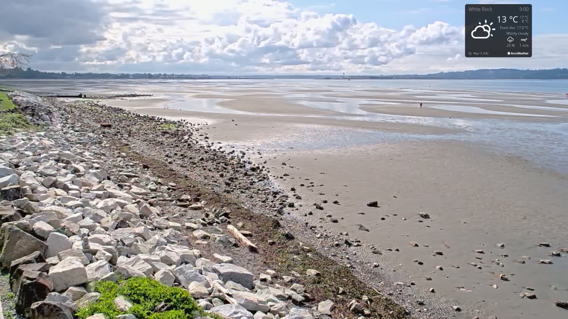 A mostly cloudy sky overlooks a rocky shoreline and a wide expanse of sandy beach at low tide.