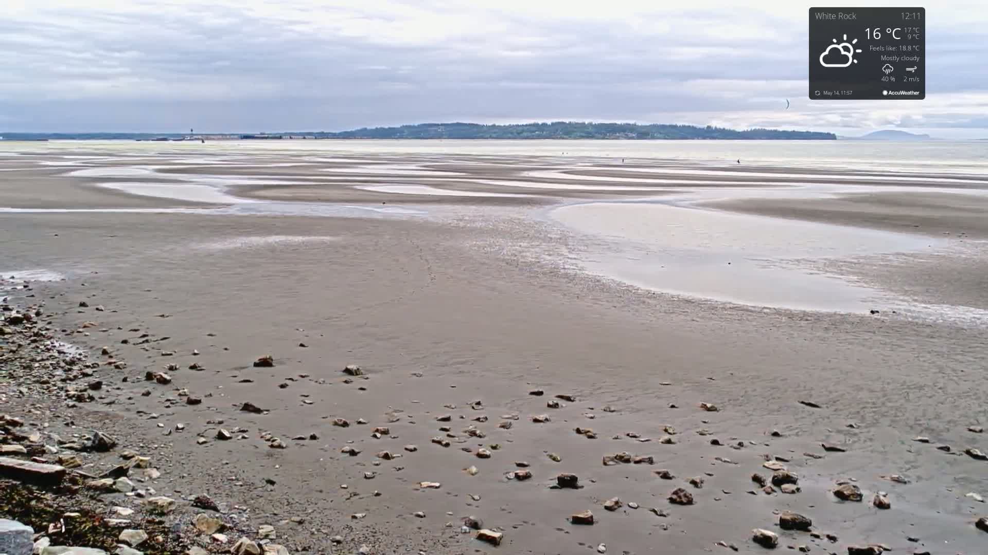 A mostly cloudy sky overlooks a wide expanse of tidal flats, strewn with small rocks near the foreground.