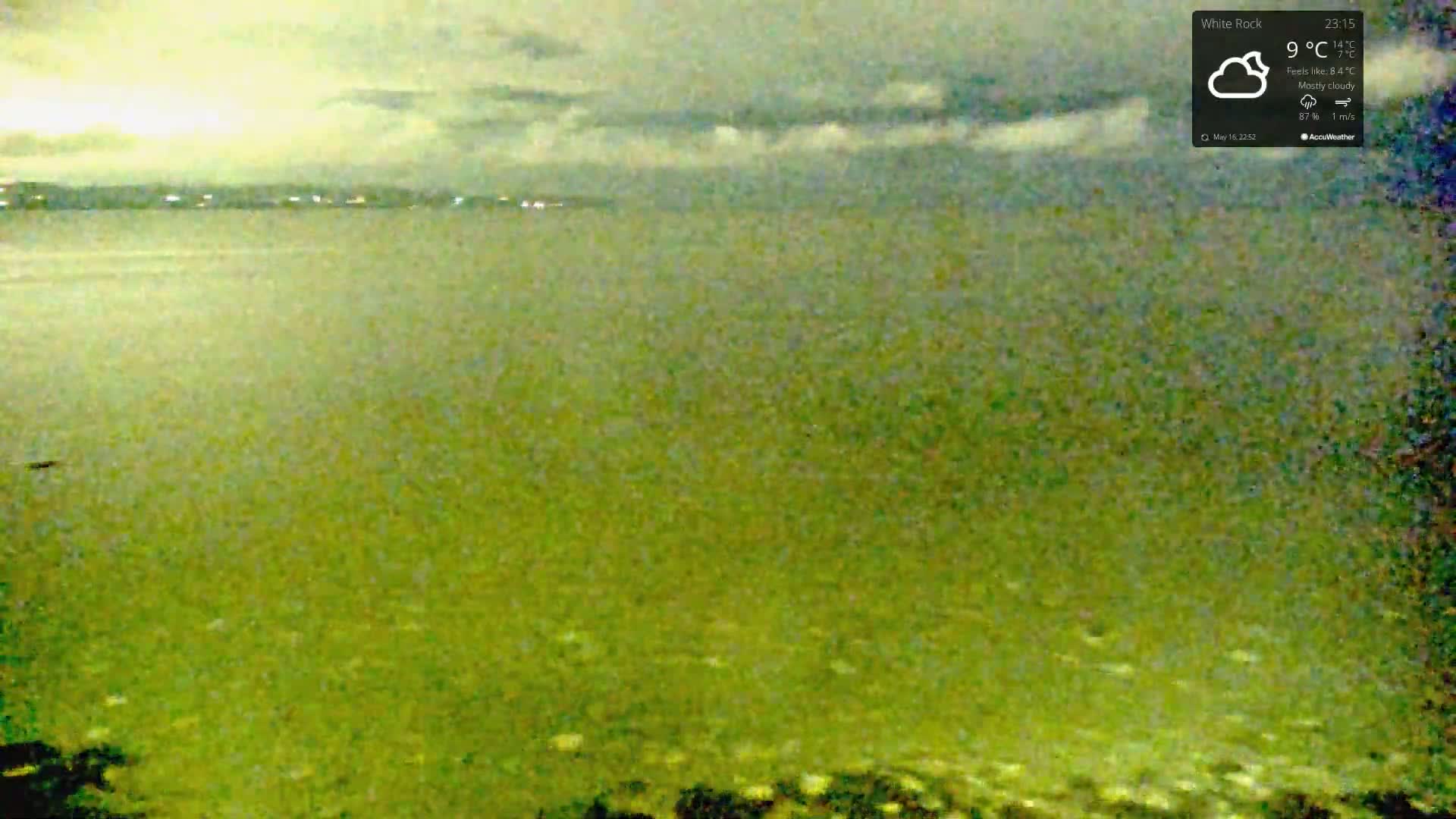 A mostly cloudy night scene shows a calm body of water under a pale sky.