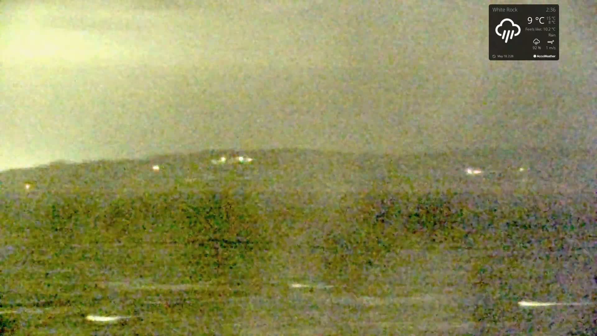 A blurry, muted green landscape is visible under a rainy, overcast sky.