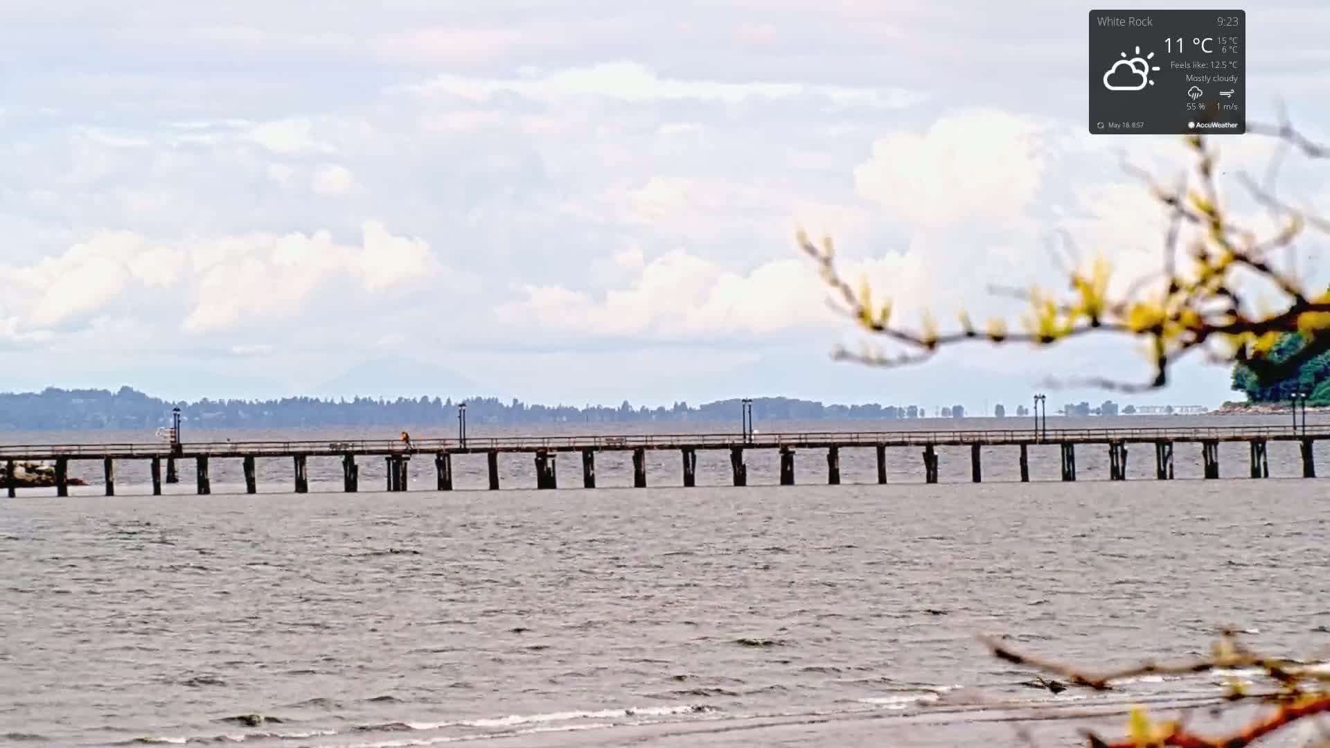 A long pier extends into a calm body of water under a mostly cloudy sky.