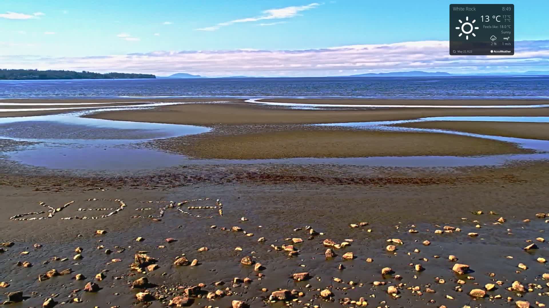 A sunny beach with tide pools and the word "PEACE" spelled out in rocks is visible, with a calm body of water and distant mountains in the background.